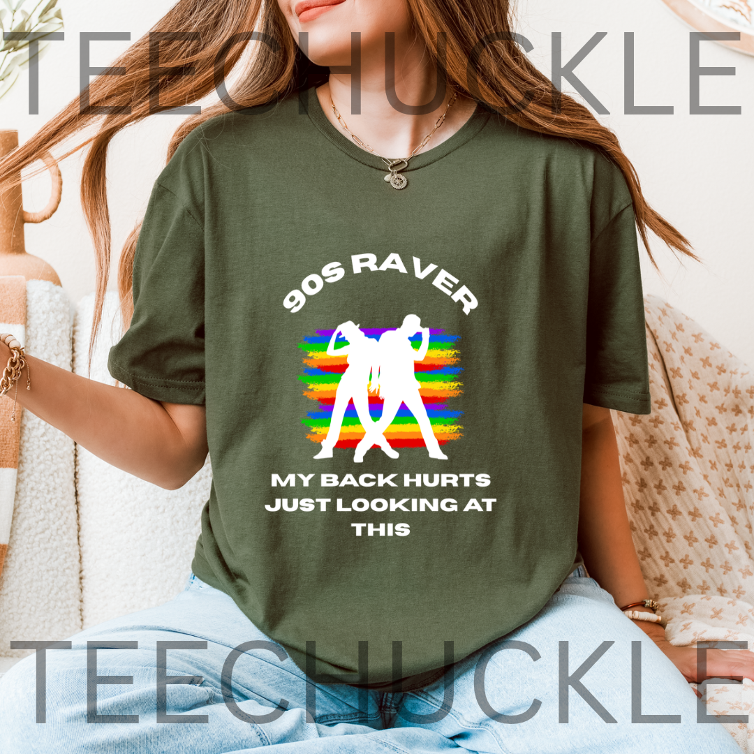 A woman wearing a green graphic t-shirt with a retro 90s theme. The shirt features white text reading '90S RAVER MY BACK HURTS JUST LOOKING AT THIS' surrounding a white silhouette of a person dancing in front of a colorful rainbow-striped background.