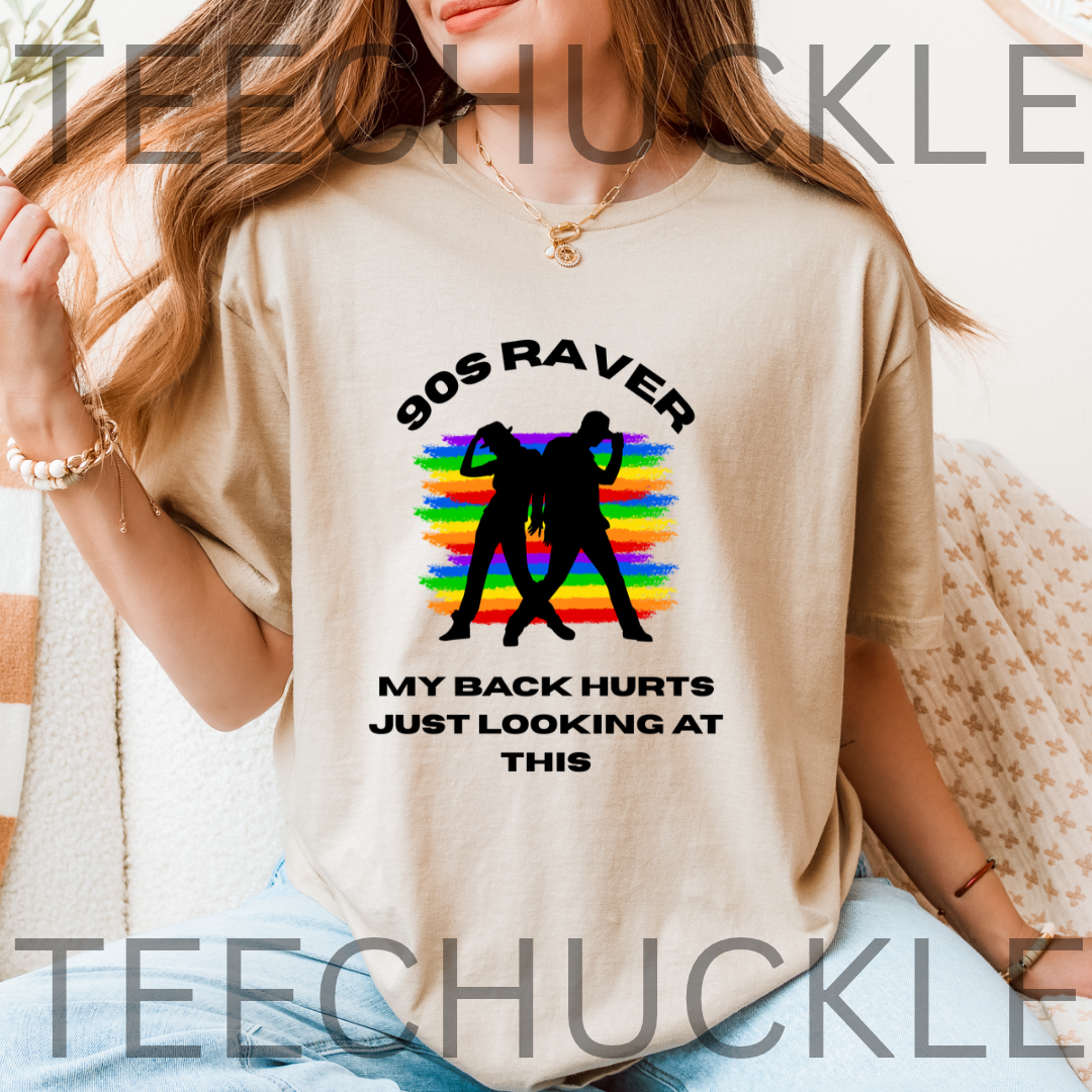 A woman wearing a sand graphic t-shirt with a black text design reading '90S RAVER MY BACK HURTS JUST LOOKING AT THIS' and a black silhouette over a rainbow striped background.