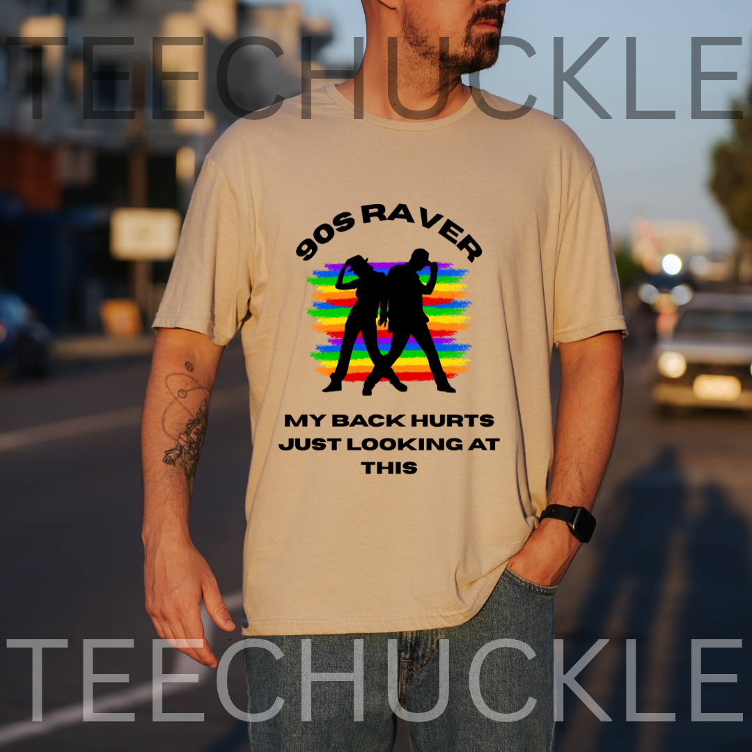 A man wearing a beige graphic t-shirt with a '90s Raver' design featuring a rainbow stripe background and black silhouette figures, with text reading 'MY BACK HURTS JUST LOOKING AT THIS'.