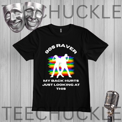 A black short-sleeve graphic t-shirt displayed on a gray wood plank background. The shirt features a white text graphic reading '90S RAVER MY BACK HURTS JUST LOOKING AT THIS' surrounding a white silhouette of a dancing figure over a colorful rainbow-striped background.