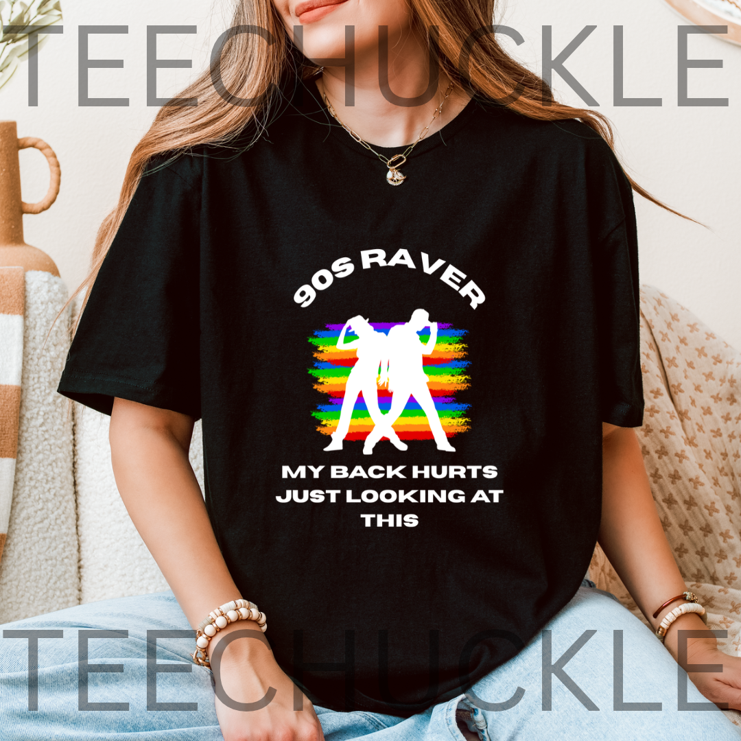 A woman wearing a black graphic t-shirt with a '90s Raver' design featuring white text and silhouettes over a rainbow background, sitting on a couch.