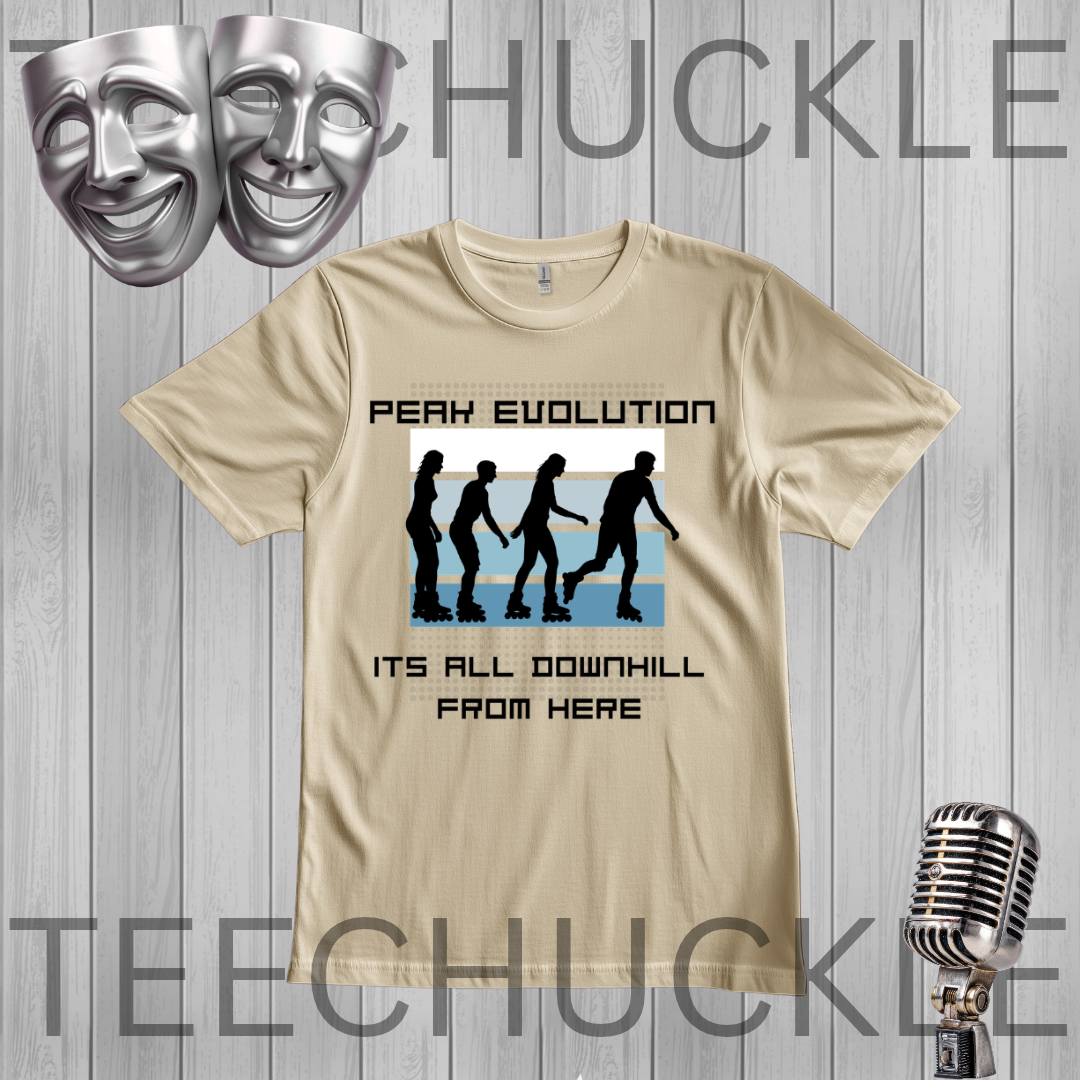 A graphic t-shirt displayed on a gray wood-plank background, featuring a 'Peaky Evolution' design with black silhouettes of figures walking downhill and the text 'ITS ALL DOWNHILL FROM HERE'. Silver theater masks and a vintage microphone are shown as decorative props