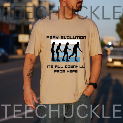 A man wearing a sand graphic t-shirt with a 'PEAK EVOLUTION' downhill silhouette design, standing outdoors on a street at sunset. 
