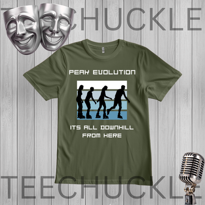 A green graphic t-shirt featuring the text 'PEAK EVOLUTION' and 'ITS ALL DOWNHILL FROM HERE' with a silhouette graphic of people skiing down a slope. The t-shirt is displayed on a gray wood-plank background with decorative silver comedy and microphone masks.