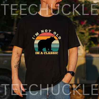 A man wearing a black graphic t-shirt with a retro sunset design and a bear silhouette, featuring the text 'I'M NOT OLD IM A CLASSIC'.