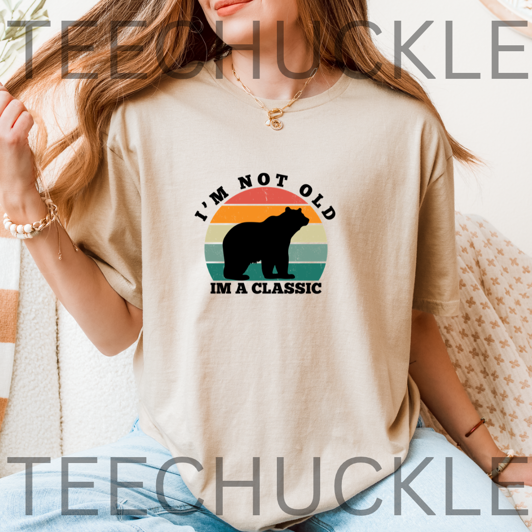A woman wearing a sand graphic t-shirt with a retro bear design and the text 'I'M NOT OLD I'M A CLASSIC'.  