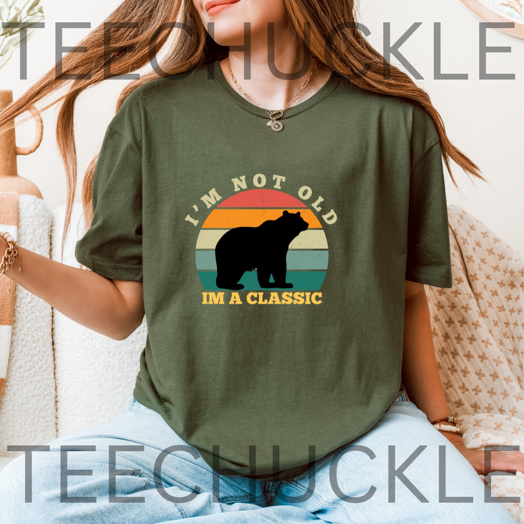 A woman wearing a green graphic t-shirt with a bear silhouette and the text 'I'M NOT OLD I'M A CLASSIC' over a retro sunset background.