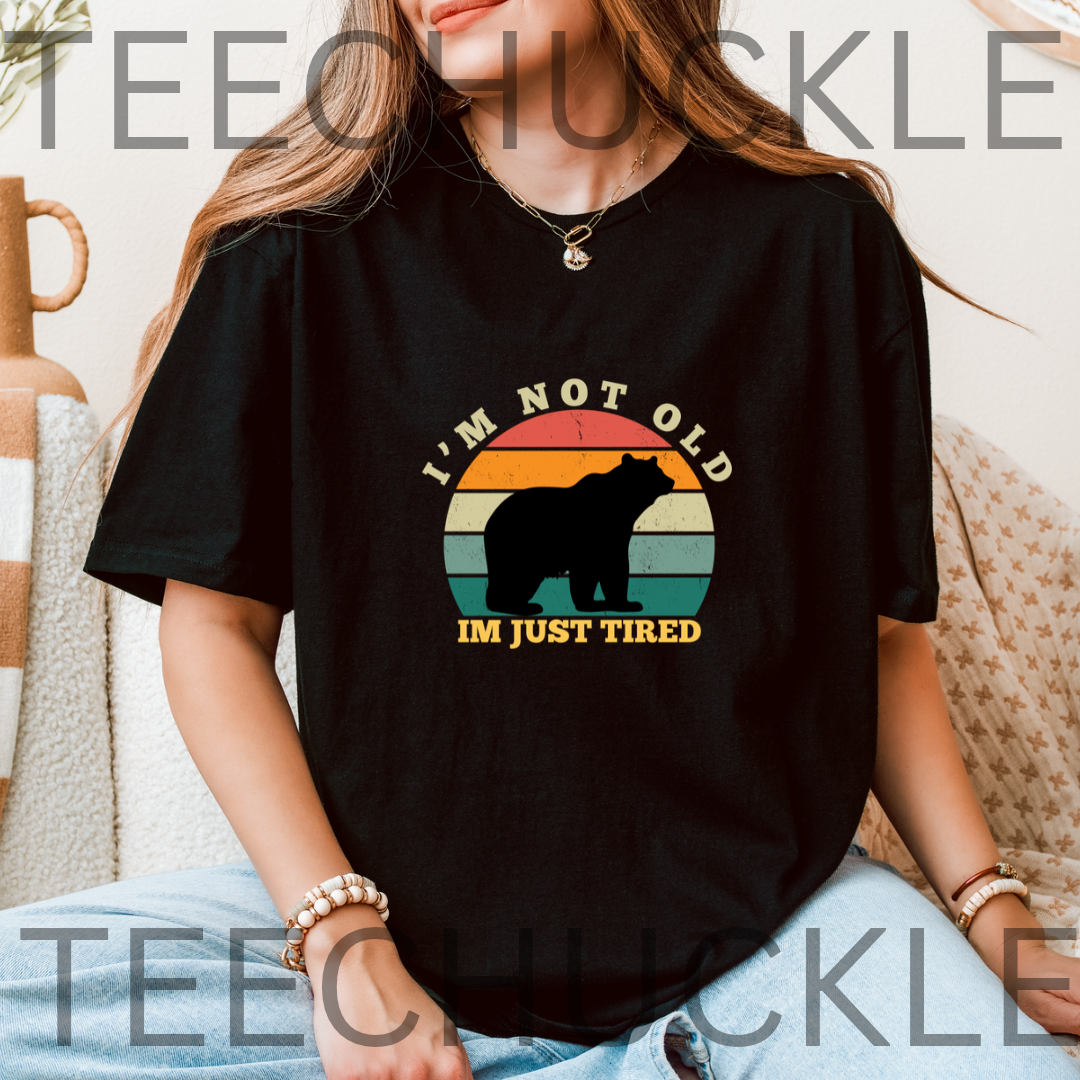 A woman wearing a black graphic t-shirt with a retro bear design and the text 'I'M NOT OLD I'M JUST TIRED'. 