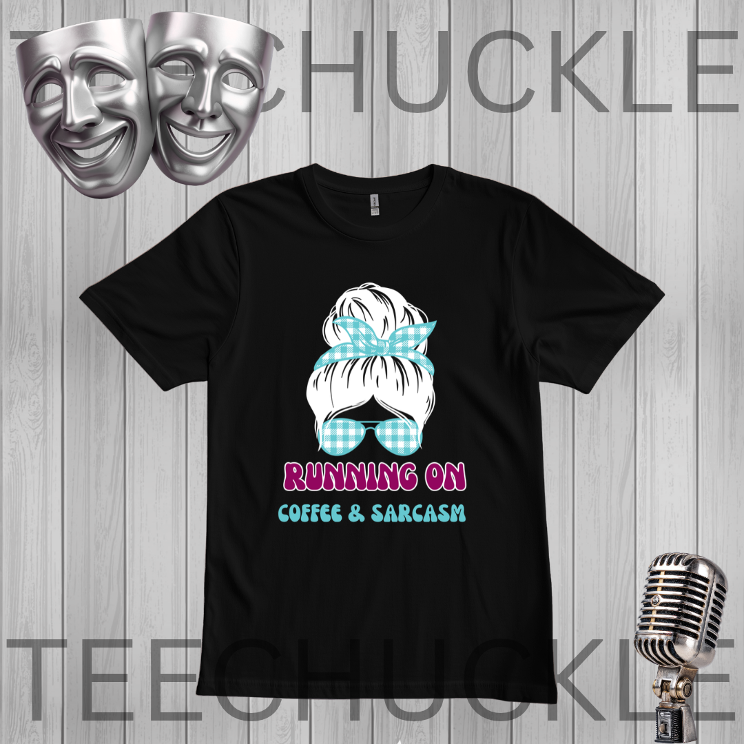 A black short-sleeve graphic t-shirt displayed on a gray wood-plank background. The graphic features a white hair bun with a light blue and white gingham bow, blue gingham sunglasses, and the text 'RUNNING ON COFFEE & SARCASM' in pink and blue.