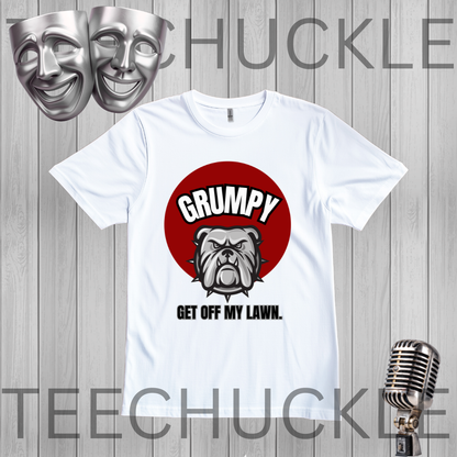 A white short-sleeve graphic T-shirt laid flat on a gray wood-plank background. The shirt has a red circular graphic with the word "GRUMPY" above a bulldog illustration and the phrase "GET OFF MY LAWN.