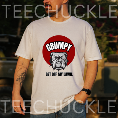 A man wearing a white graphic t-shirt with a red circular bulldog design and the text 'GRUMPY GET OFF MY LAWN.' The background is an outdoor setting with a blurred car,