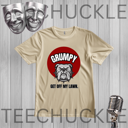 A sand graphic t-shirt featuring a red circle with a bulldog and the text 'GRUMPY GET OFF MY LAWN.' displayed on a gray wood plank background with theatrical masks, a vintage microphone, 