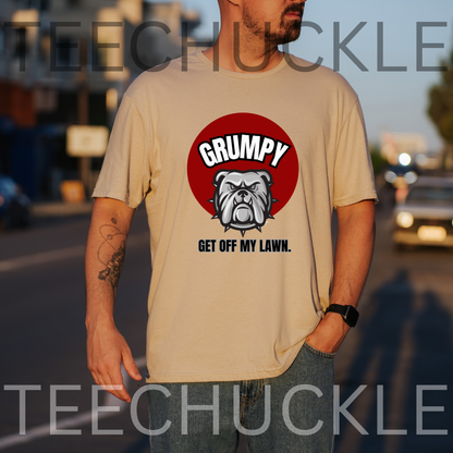 A man wearing a sand graphic t-shirt with a red circular bulldog design and the text 'GRUMPY GET OFF MY LAWN.' The photo is taken outdoors on a street at sunset, 