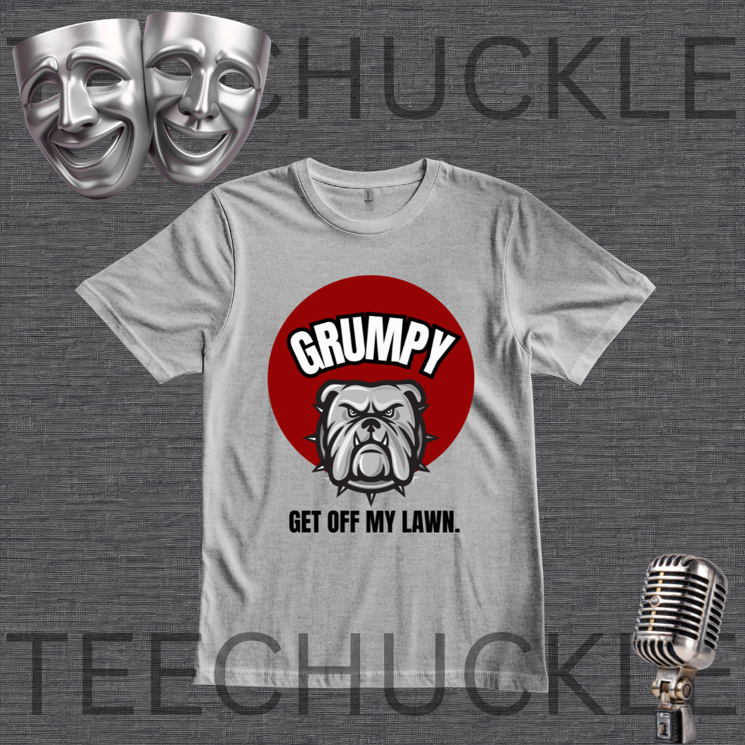 A gray graphic t-shirt featuring a red circle with the word 'GRUMPY' above a bulldog illustration and the phrase 'GET OFF MY LAWN.' The shirt is displayed on a dark gray textured background with theatrical comedy masks in the top-left and a vintage microphone in the bottom-right.