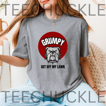 A woman wearing a gray graphic t-shirt with a red circular bulldog design and the text 'GRUMPY GET OFF MY LAWN.'