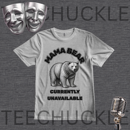 A gray graphic t-shirt featuring a black and white illustration of a bear with the text 'MAMA BEAR' above and 'CURRENTLY UNAVAILABLE' below. The t-shirt is displayed on a dark gray textured background with decorative props including two silver theater masks, a vintage microphone