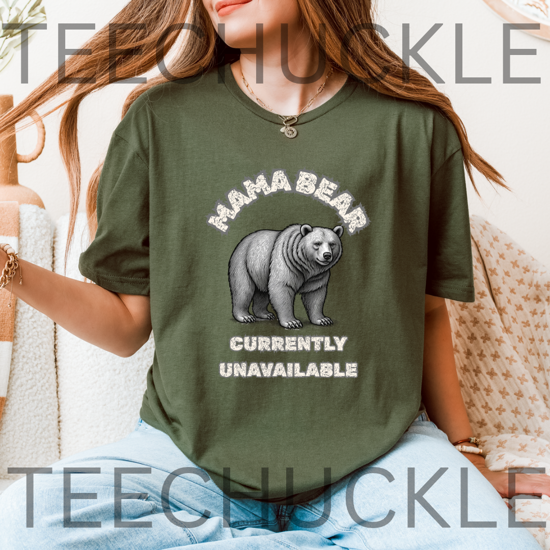A woman wearing a green graphic t-shirt with a 'MAMA BEAR CURRENTLY UNAVAILABLE' design featuring a bear illustration, set against a cozy indoor background with a blanket.