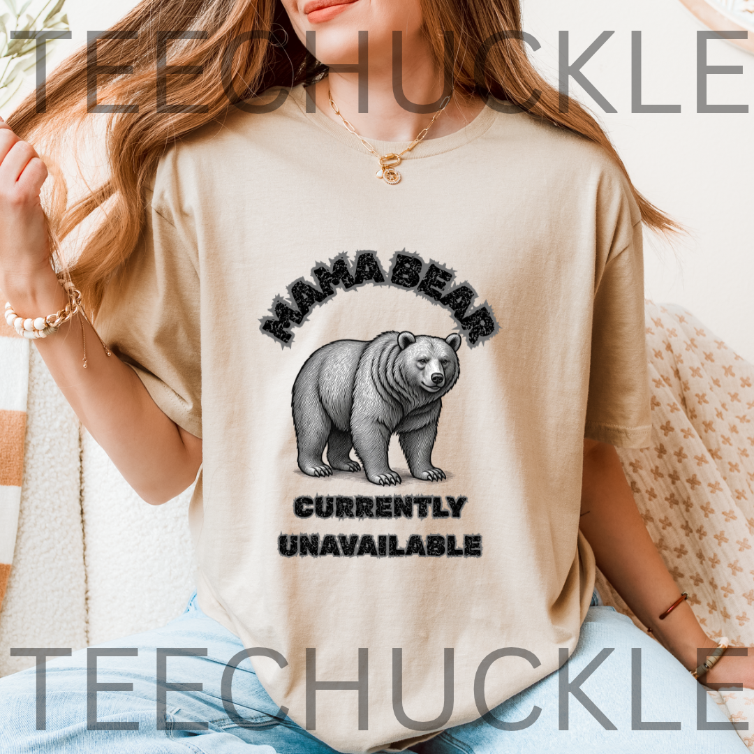 A woman wearing a beige graphic t-shirt with a black bear illustration and the text 'MAMA BEAR CURRENTLY UNAVAILABLE'. 