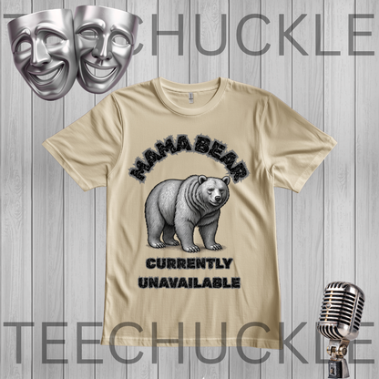 A sand graphic t-shirt featuring a black and white polar bear illustration with the text 'MAMA BEAR' and 'CURRENTLY UNAVAILABLE'. The t-shirt is displayed on a gray wood-plank background with decorative silver theater masks and a vintage microphone