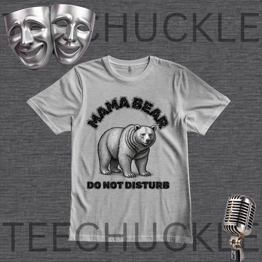 A gray graphic t-shirt featuring a black and white illustration of a mama bear with the text 'MAMA BEAR DO NOT DISTURB'. The t-shirt is displayed on a dark gray textured background with theatrical comedy and tragedy masks in the top-left corner and a vintage microphone in the bottom-right corner.