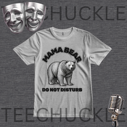 A gray graphic t-shirt featuring a black and white illustration of a mama bear with the text 'MAMA BEAR DO NOT DISTURB'. The t-shirt is displayed on a dark gray textured background with theatrical comedy and tragedy masks in the top-left corner and a vintage microphone in the bottom-right corner.