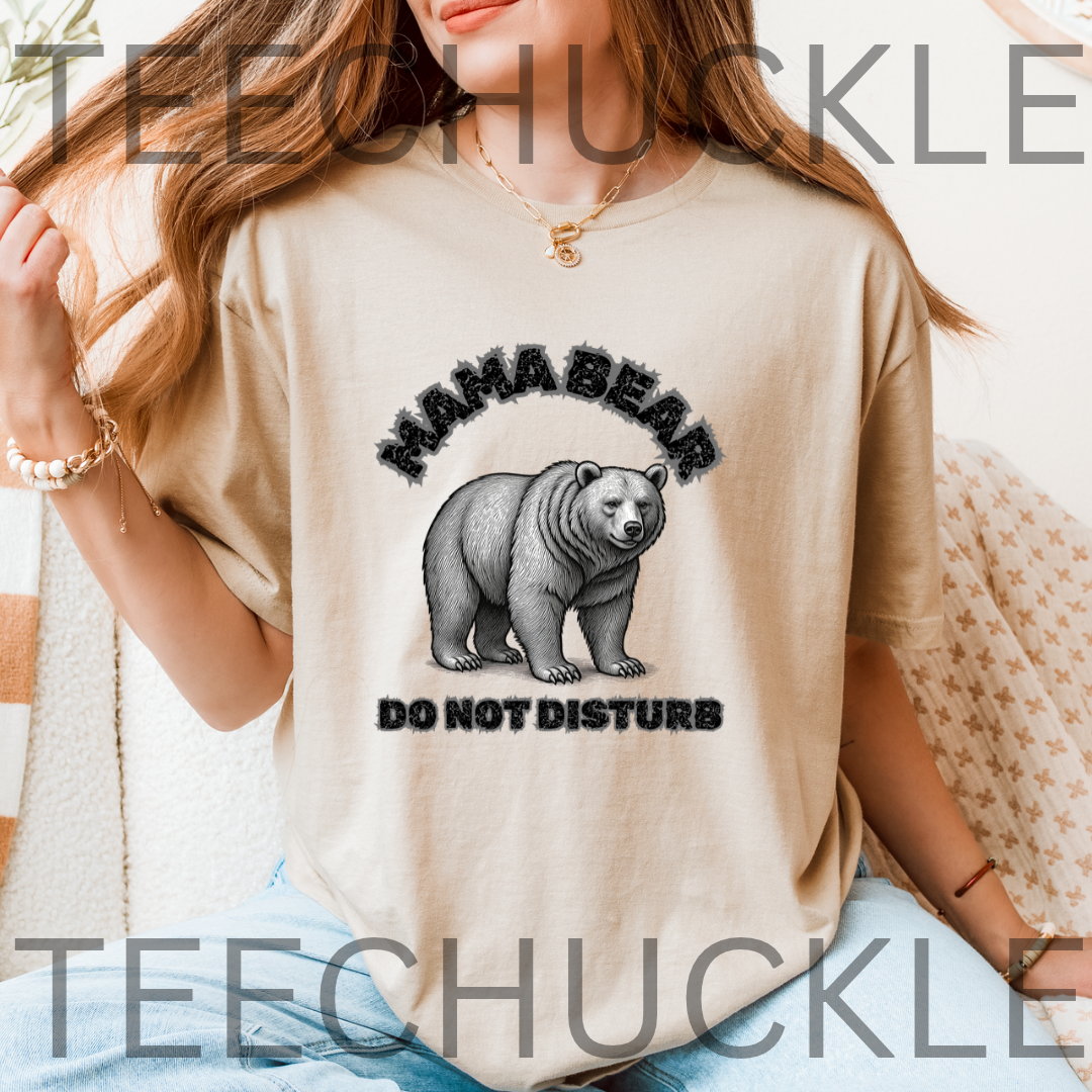 A woman wearing a sand graphic t-shirt with a black and gray 'MAHA BEAR DO NOT DISTURB' design