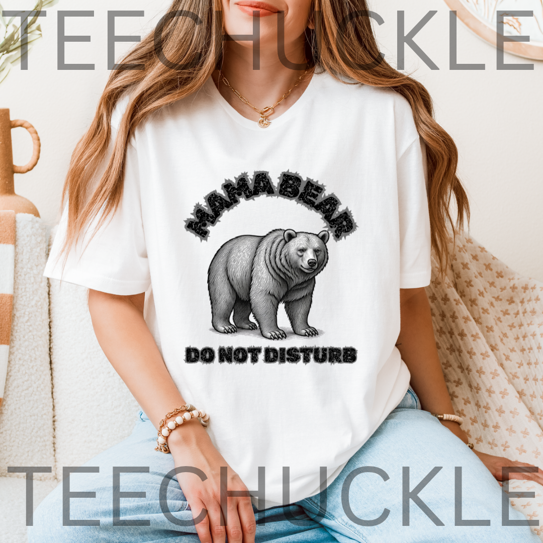 A woman wearing a white graphic t-shirt with a black and gray 'MAMA BEAR DO NOT DISTURB' design featuring a bear illustration.