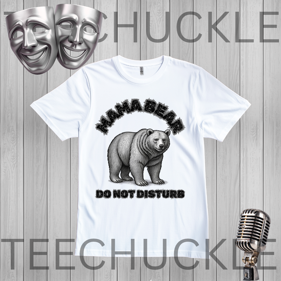 A white graphic t-shirt featuring a black and gray illustration of a bear with the text 'MAMA BEAR DO NOT DISTURB'. The t-shirt is displayed on a gray wood-plank background with decorative props including two silver theater masks at the top left, a vintage silver microphone at the bottom right