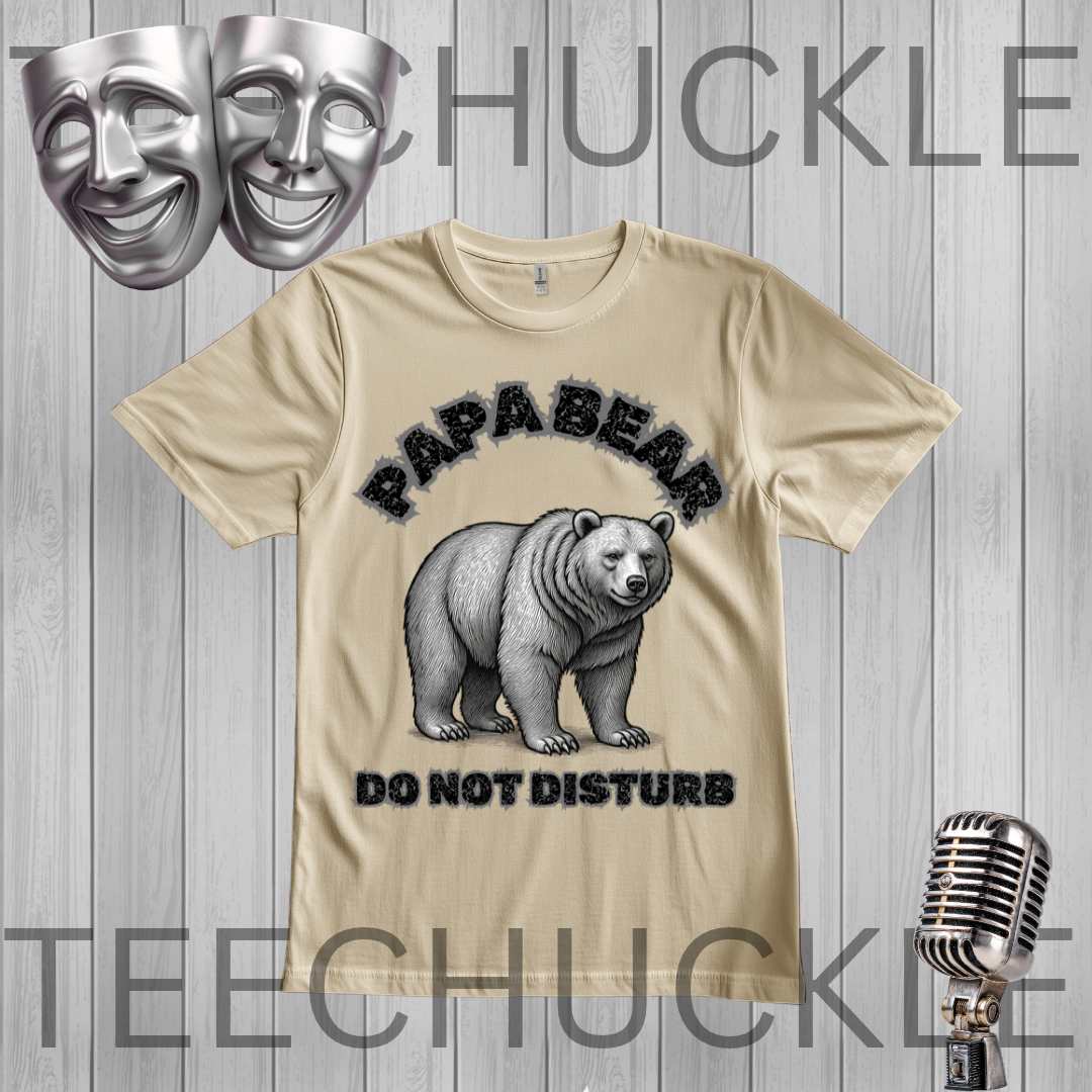 A sand graphic t-shirt featuring a polar bear illustration with the text 'PAPABEAR DO NOT DISTURB'. The t-shirt is displayed on a gray wood-plank background with decorative props including two silver theater masks, a vintage microphone
