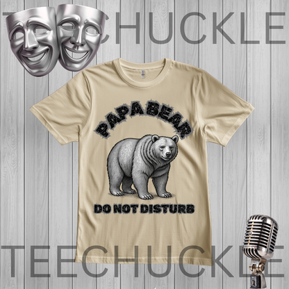 A sand graphic t-shirt featuring a polar bear illustration with the text 'PAPABEAR DO NOT DISTURB'. The t-shirt is displayed on a gray wood-plank background with decorative props including two silver theater masks, a vintage microphone
