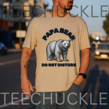 A man wearing a sand graphic t-shirt with a black and white polar bear illustration and the text 'PAPA BEAR DO NOT DISTURB'. The background is a blurred street scene at sunset
