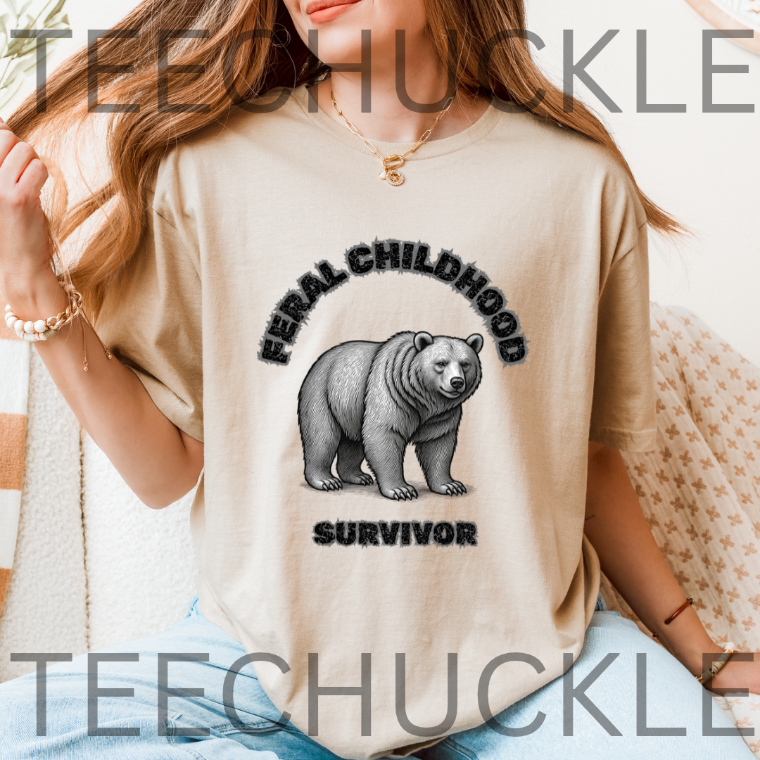 A woman wearing a sand graphic t-shirt with a black illustration of a bear and the text 'FERAL CHILDHOOD SURVIVOR'. 