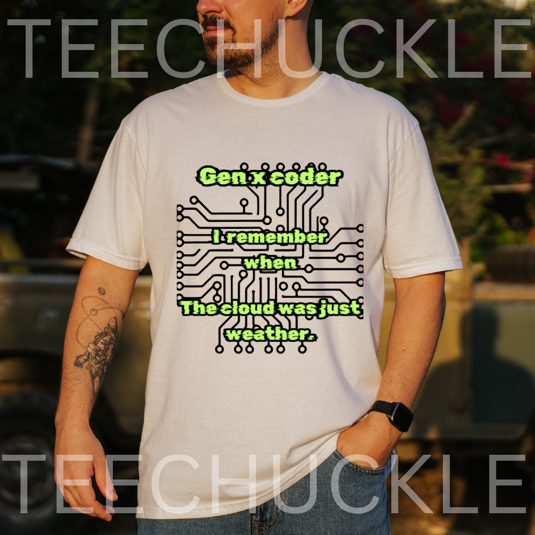 A man wearing a white graphic t-shirt with a green and black circuit board design and the text 'Gen x coder I remember when The cloud was just weather.' The background is a blurred outdoor setting