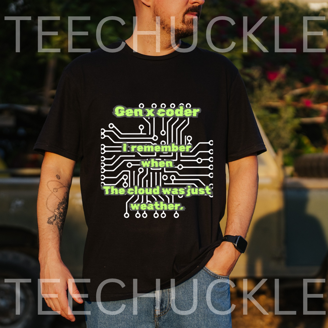A man wearing a black graphic t-shirt with a green and white circuit board design and the text 'Gen X coder I remember when The cloud was just weather.' The background is an outdoor blurred setting