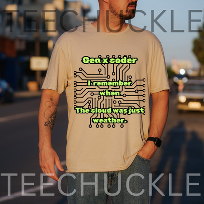 A man wearing a sand graphic t-shirt with a green and black circuit board design and the text 'Gen x coder I remember when The cloud was just weather.' The background is a blurred street scene at sunset