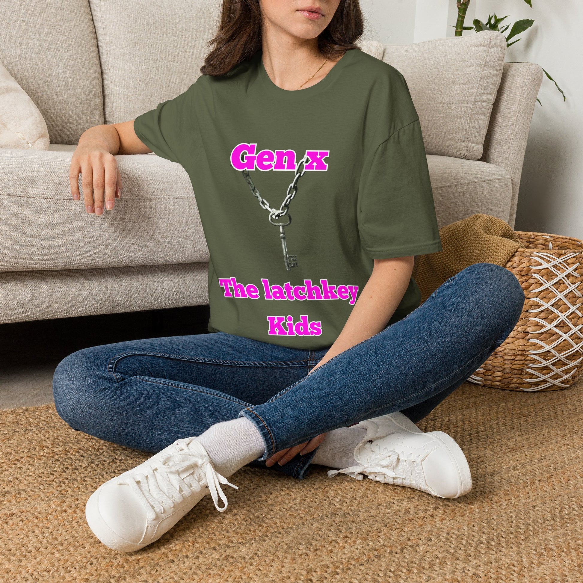 A woman sitting cross-legged on a woven rug in front of a beige sofa, wearing a green graphic t-shirt with pink text reading 'Gen X The latchkey Kids' and blue jeans.