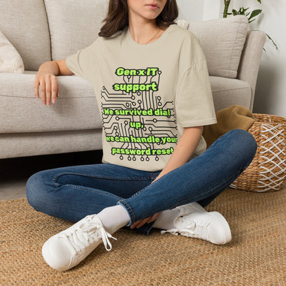A woman sitting cross-legged on a woven rug in front of a light beige sofa, wearing a sand graphic t-shirt with green text and circuit board graphics, blue jeans, and white sneakers.