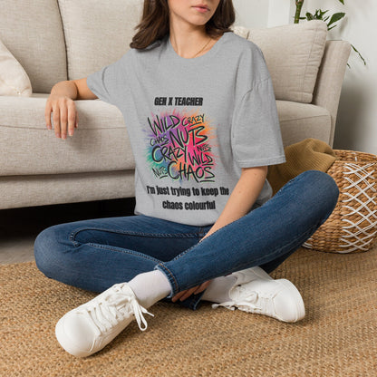 A woman sitting on a woven rug in front of a beige sofa, wearing a gray graphic t-shirt with colorful text that reads 'GEN X TEACHER WILD CRASH NUTS CRAZE CHAOS' and 'I'm just trying to keep the chaos colourful'.