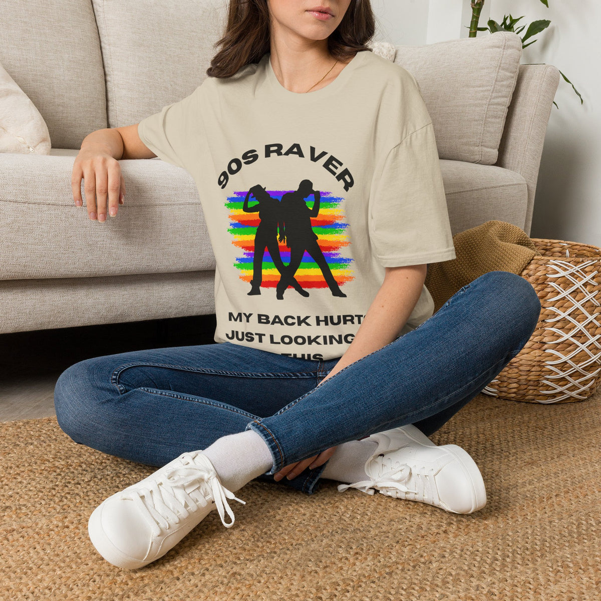 A sand graphic t-shirt featuring a black silhouette of two people dancing in front of a rainbow stripe pattern, with the text '90S RAVER MY BACK HURTS JUST LOOKING AT THIS'. 