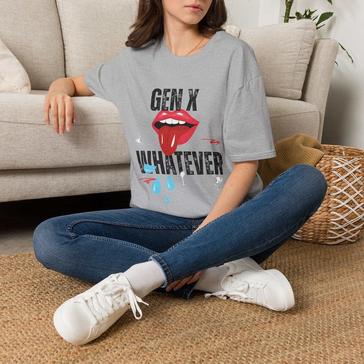 A woman sat on a rug next to a couch wearing a grey short-sleeve graphic t-shirt featuring the text 'GEN X WHATEVER' in black, with a graphic of red lips.