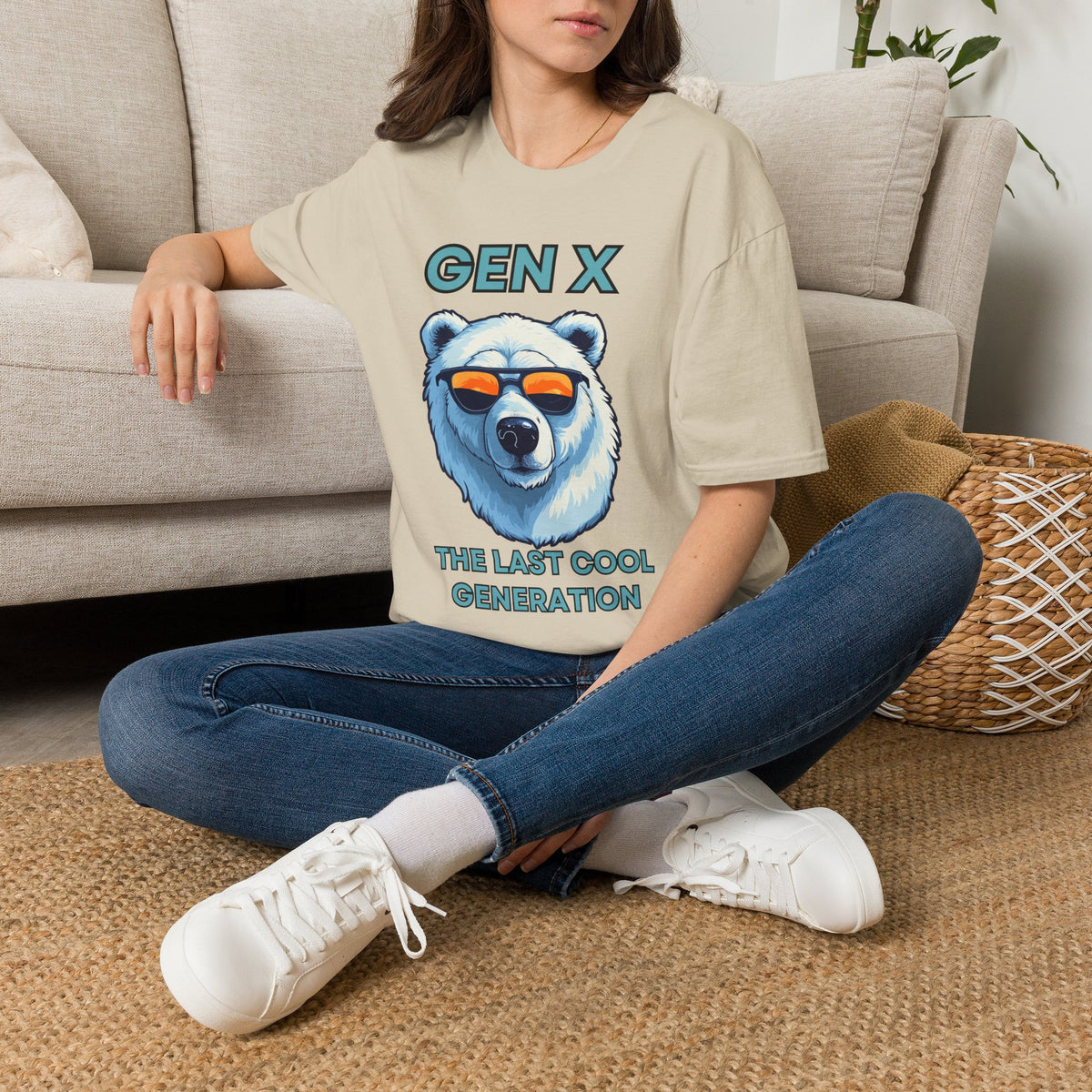 A woman sat on a rug next to a couch wearing a sand short-sleeve graphic T-shirt, with blue text reading 'Gen x' and 'The last cool generation' a  polar bear illustration.