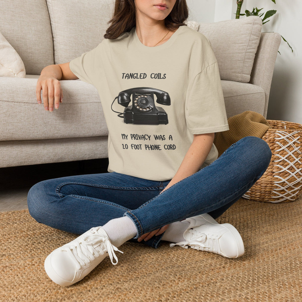 A sand short-sleeve graphic T-shirt The shirt has a black printed design featuring a vintage rotary telephone and the text 'TANGLED COILS' above it and 'MY PRIVACY WAS A 20 FOOT PHONE CORD' below it.