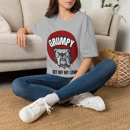 A woman sitting on a woven rug in front of a beige sofa, wearing a gray graphic t-shirt with a red circle and bulldog design that reads 'GRUMPY GET OFF MY LAWNS'.