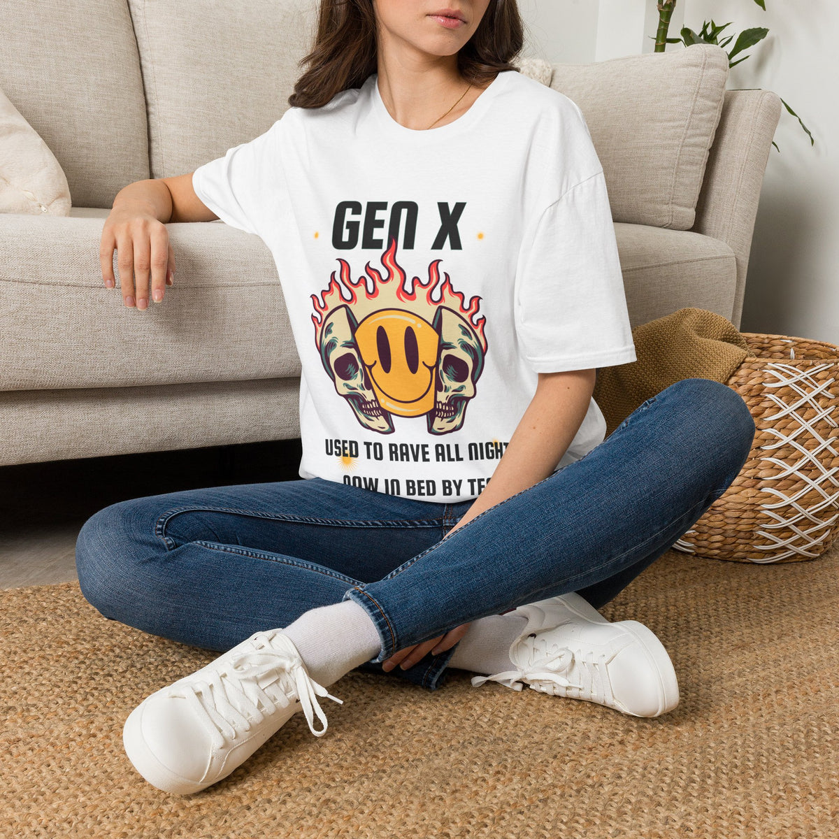 A white short-sleeve graphic t-shirt  The shirt features a 'Gen X' meme graphic with two skulls in sunglasses, a yellow smiley face inside a flame, and text that reads 'USED TO RAVE ALL NIGHT, NOW IN BED BY TEN'.