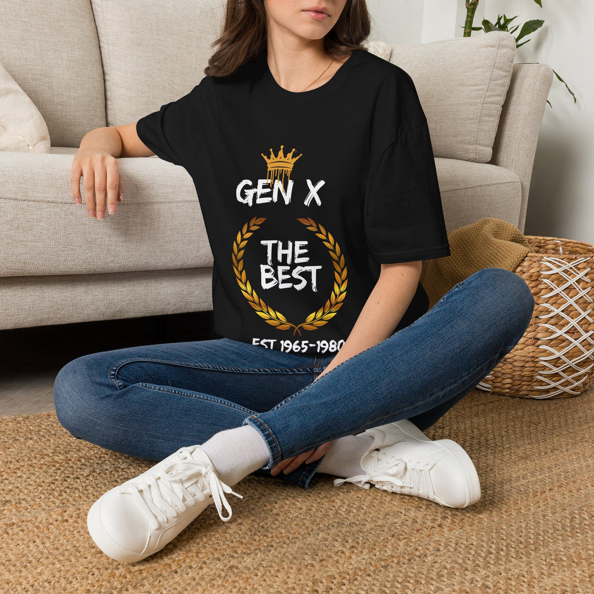 Person wearing a Black  t-shirt with a crown and gold wreath graphic and Gen X The Best text in white, sitting on a carpeted floor.