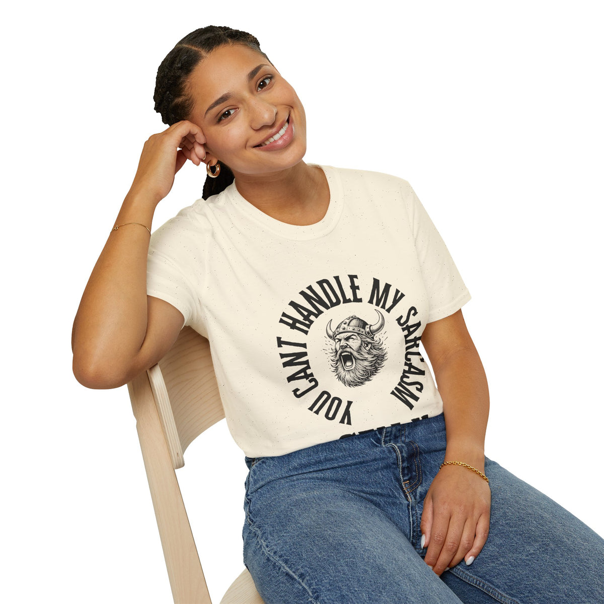 A woman sitting on a light wood chair wearing a cream-colored graphic t-shirt with a black viking design and the text 'YOU CAN'T HANDLE MY SARCASM'.