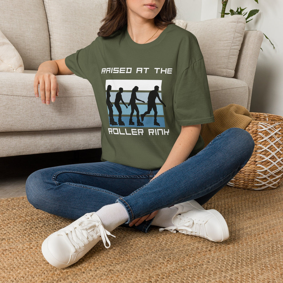 Person wearing a green t-shirt with a graphic of roller skaters and the text " raised at the roller rink", sitting on the floor in a living room.