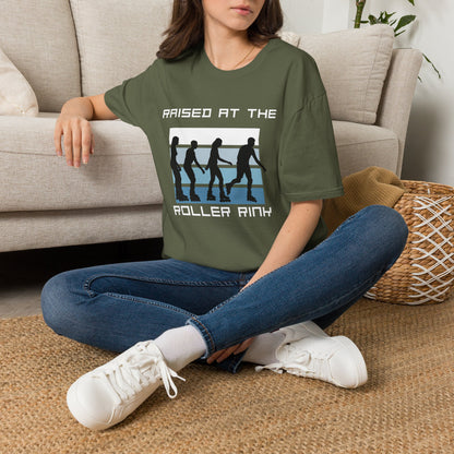 Person wearing a green t-shirt with a graphic of roller skaters and the text " raised at the roller rink", sitting on the floor in a living room.