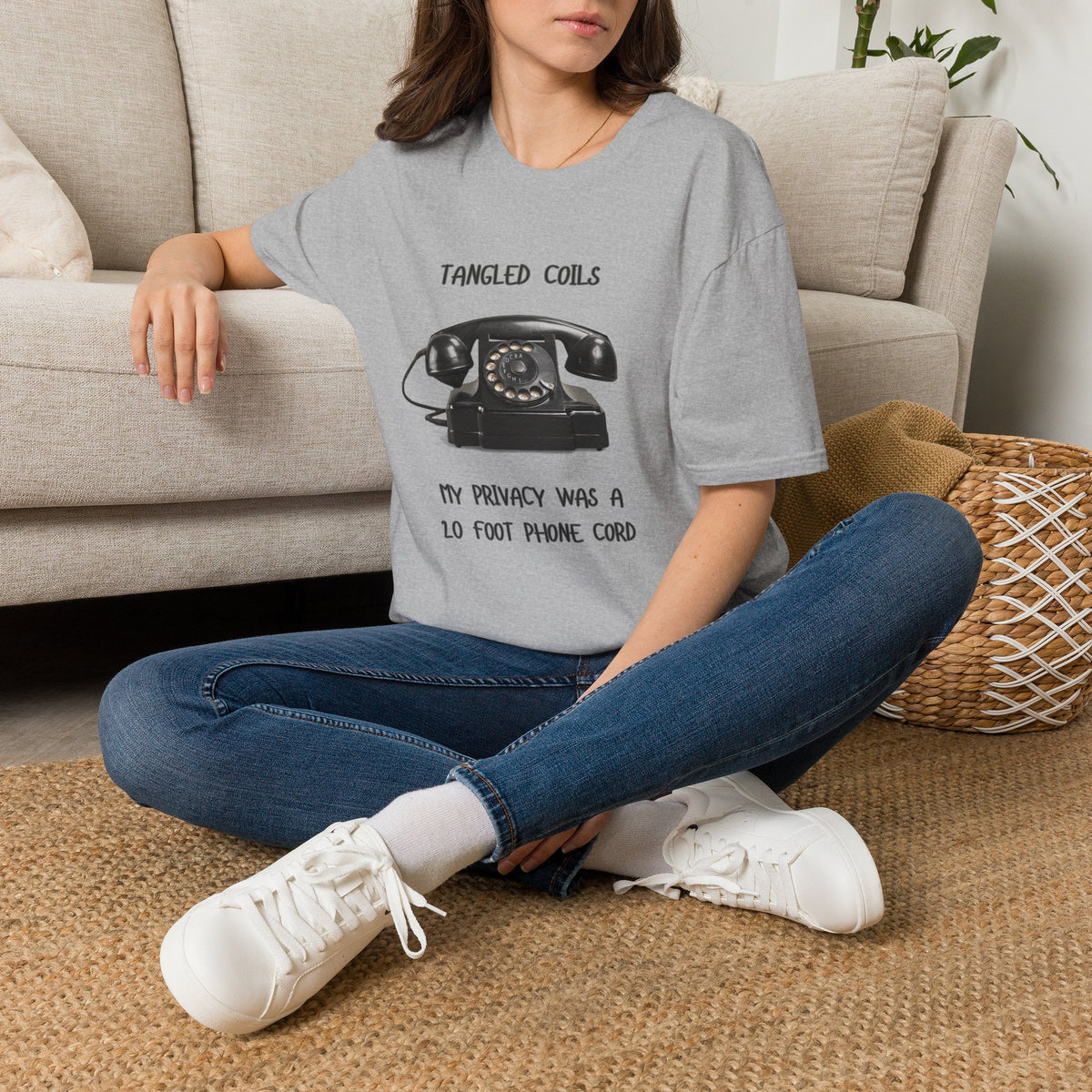 A grey short-sleeve graphic T-shirtThe shirt has a black printed design featuring a vintage rotary telephone and the text 'TANGLED COILS' above it and 'MY PRIVACY WAS A 20 FOOT PHONE CORD' below it.