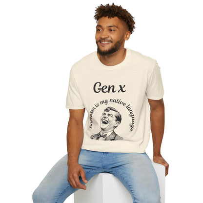 A man wearing a cream-colored graphic t-shirt with a black print that reads 'Gen x' and 'Sarcasm is my native language' with an illustration of a laughing man, paired with light blue jeans, sitting on a white block against a white background.